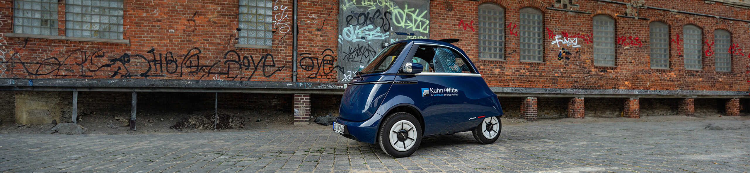 Microlino steht vor urbanem Gebäude.