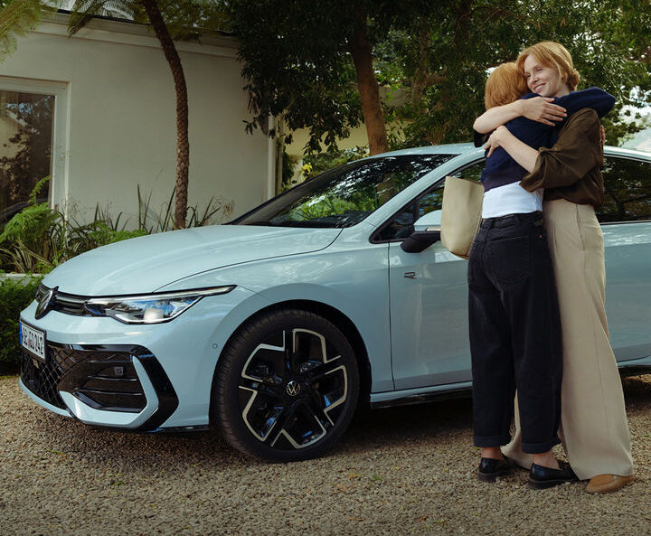 Zwei Personen umarmen sich neben einem VW Golf.